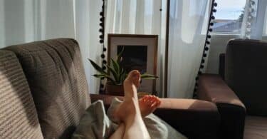 Pernas femininas cruzadas sobre um sofá. Em seu colo, um livro aberto.