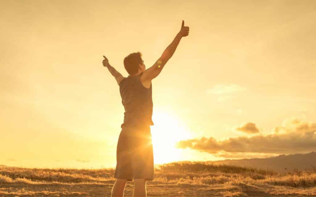 Um homem de braços erguidos e realizando, com as mãos, um gesto de "positivo".