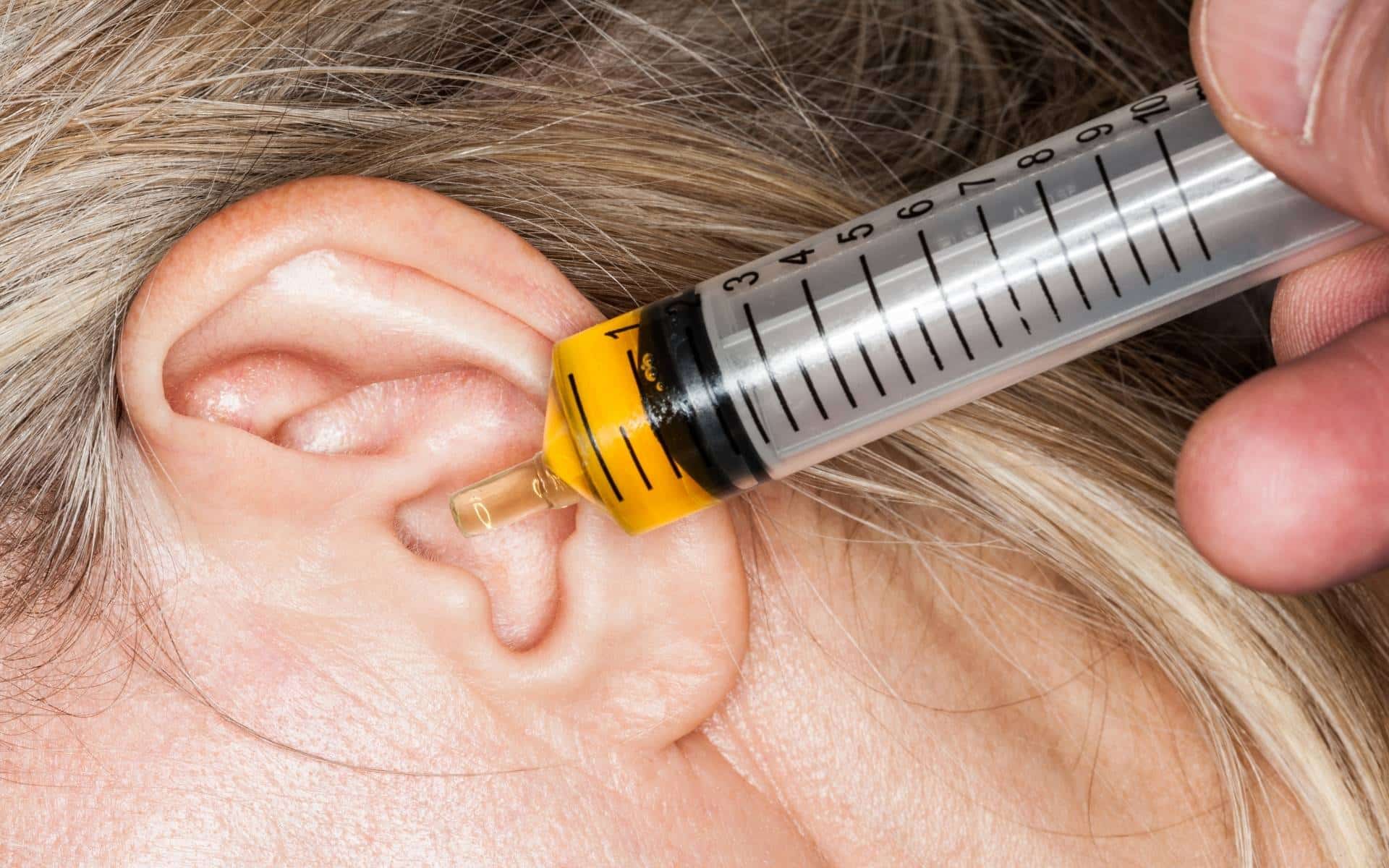 Uma mulher utilizando uma seringa no seu ouvido.