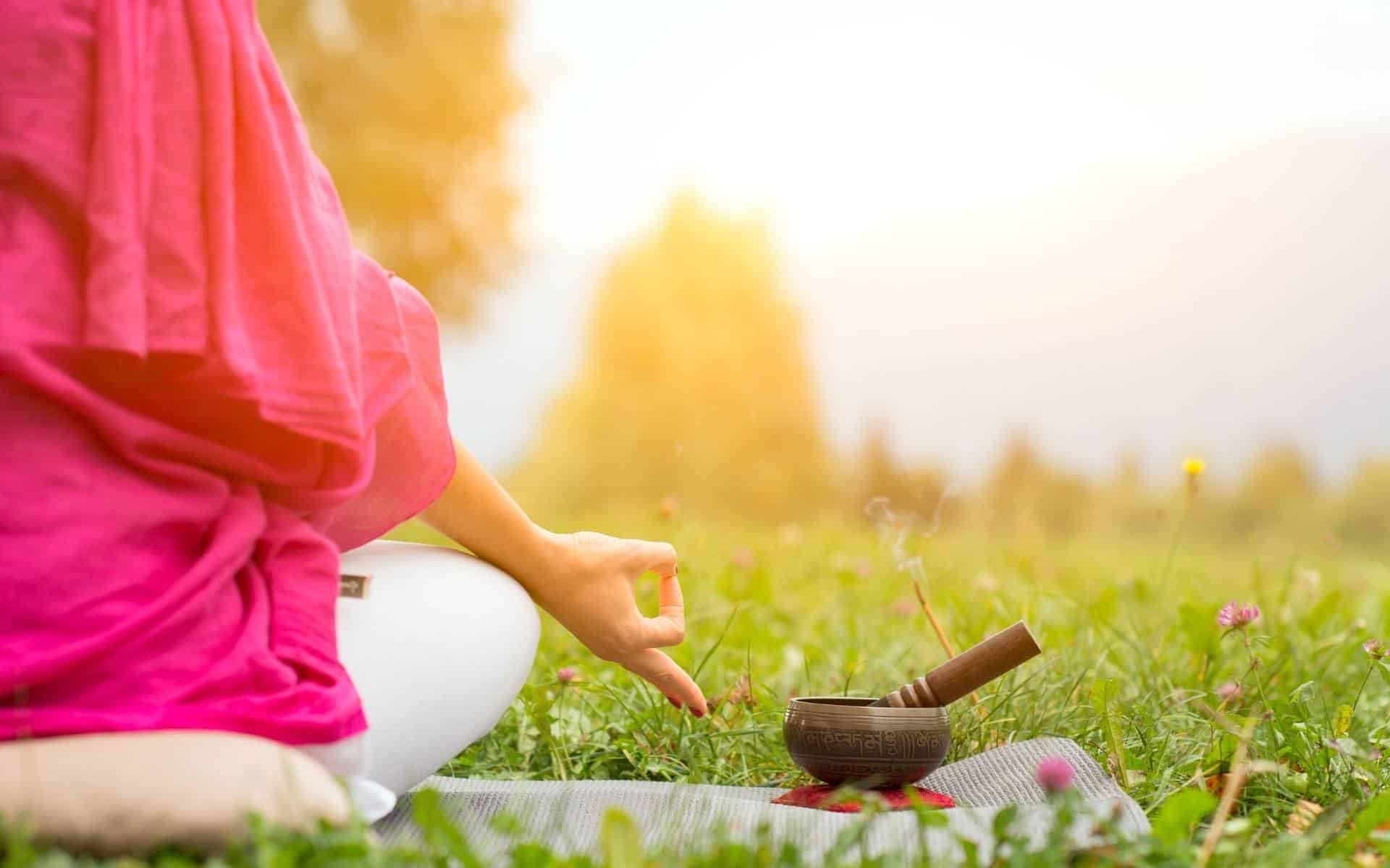 Uma pessoa meditando num gramado verde.