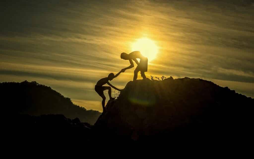 Um homem ajudando outro homem a escalar o pico de uma montanha.