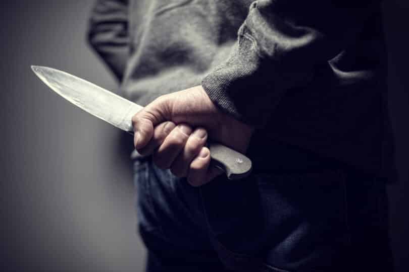 homem segurando uma faca com a mão atrás das costas