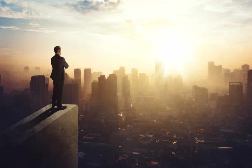 Homem olhando a cidade do alto representando alguém ambicioso que conquistou seus objetivos