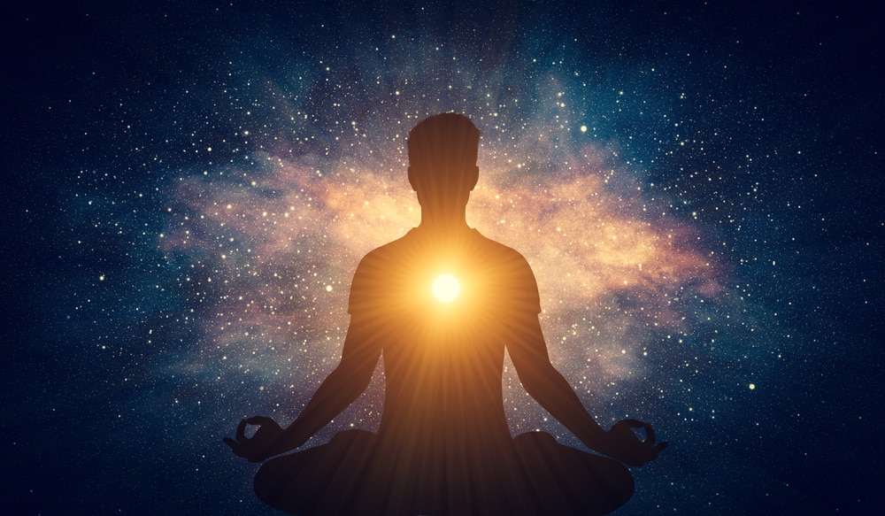 Silhueta de homem meditando no meio de uma galáxia, com um sol brilhando no centro de seu peito