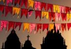 Diversas bandeiras de festa junina penduradas no ar livre com uma igreja ao fundo