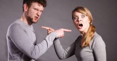 Um homem e uma mulher raivosos. Ambos apontam, um ao outro, seus dedos indicadores.