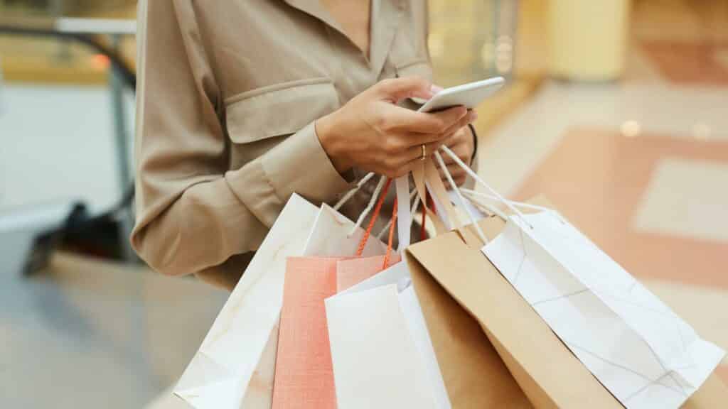 Uma mulher segurando várias sacolas de compra enquanto utiliza um celular.
