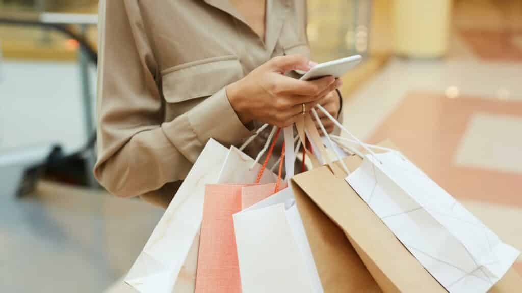 Uma mulher segurando várias sacolas de compra enquanto utiliza um celular.