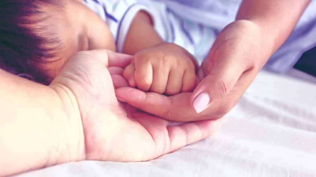 Uma mão masculina e uma mão feminina suportando a mão de um bebê.