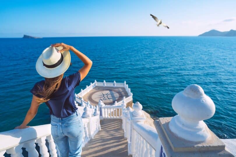 Uma mulher com um chapéu observando o mar.