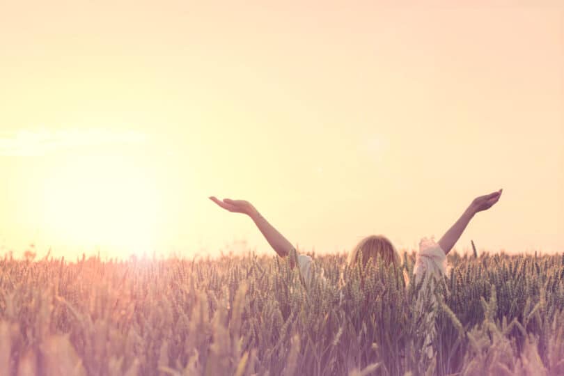 Uma mulher de braços erguidos em meio a um campo repleto de grama.