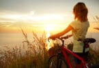 Uma mulher com uma bicicleta. Ela contempla um sol nascente.