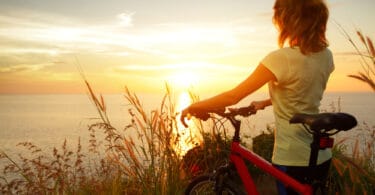 Uma mulher com uma bicicleta. Ela contempla um sol nascente.