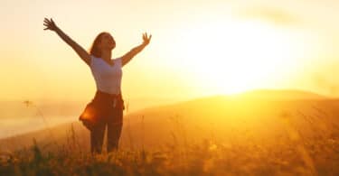 Uma mulher de braços erguidos em meio a um pôr do sol.