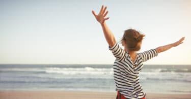Uma mulher de braços erguidos em meio a uma praia.