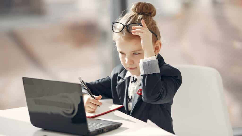 Uma jovem garota de terno utilizando um notebook e escrevendo num caderno.