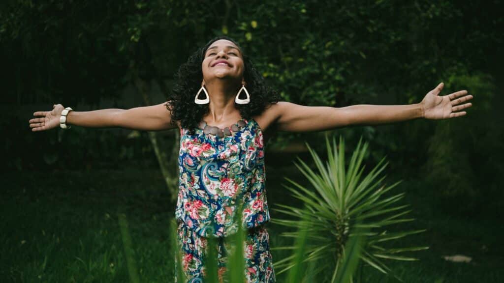 Uma mulher de braços erguidos no meio de uma floresta.