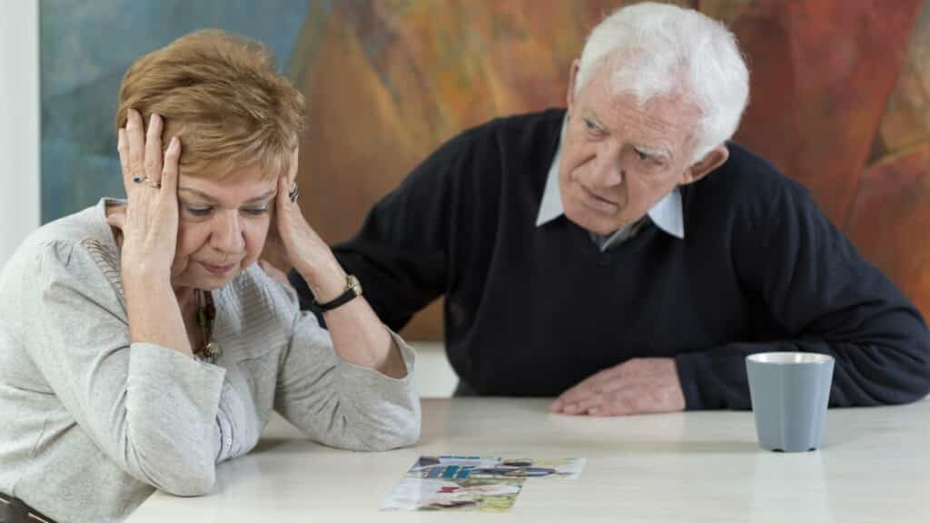 À mesa, uma mulher e um homem. A mulher coloca as suas mãos na cabeça dela.