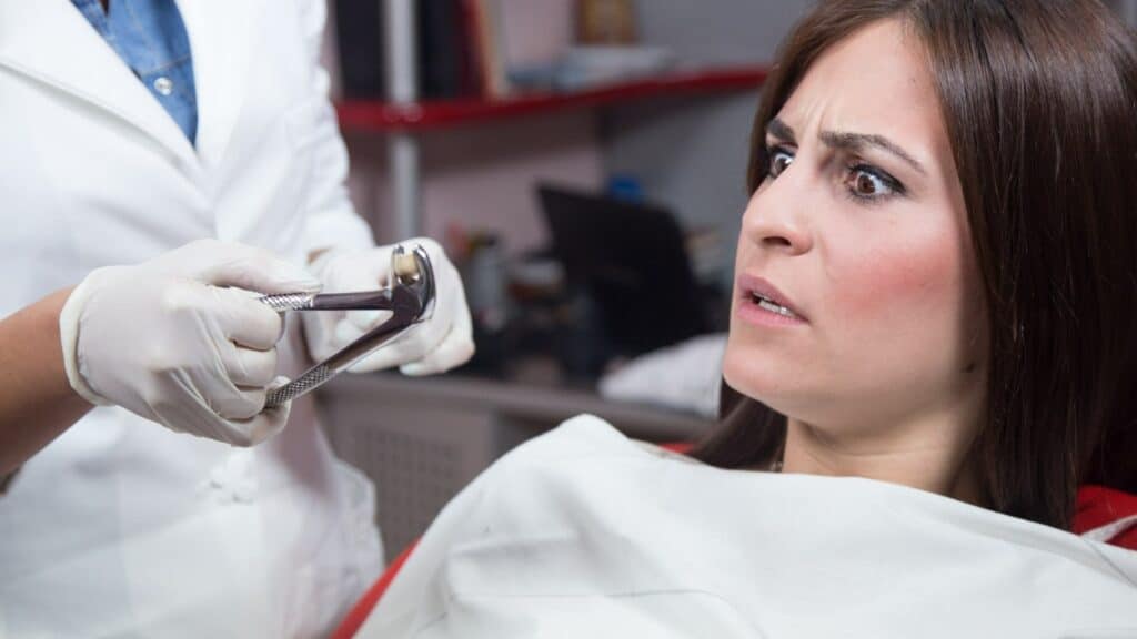 Uma mulher com uma expressão de assustada. Ao lado dela, um dentista segurando um alicate.