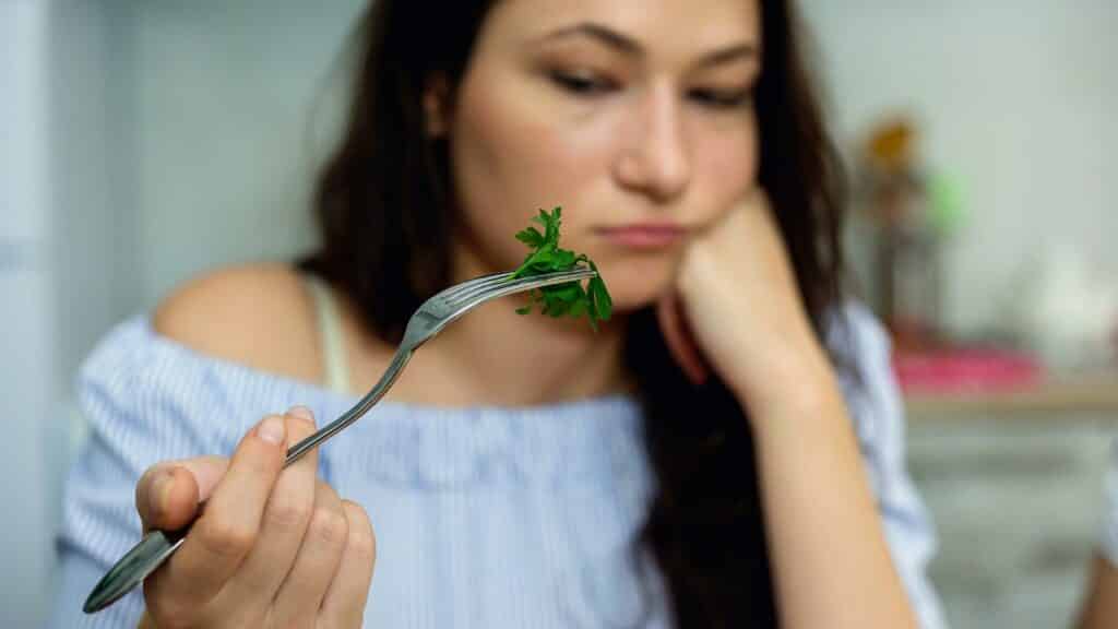 Uma mulher segurando um garfo. Neste, um pedaço de cheiro-verde.