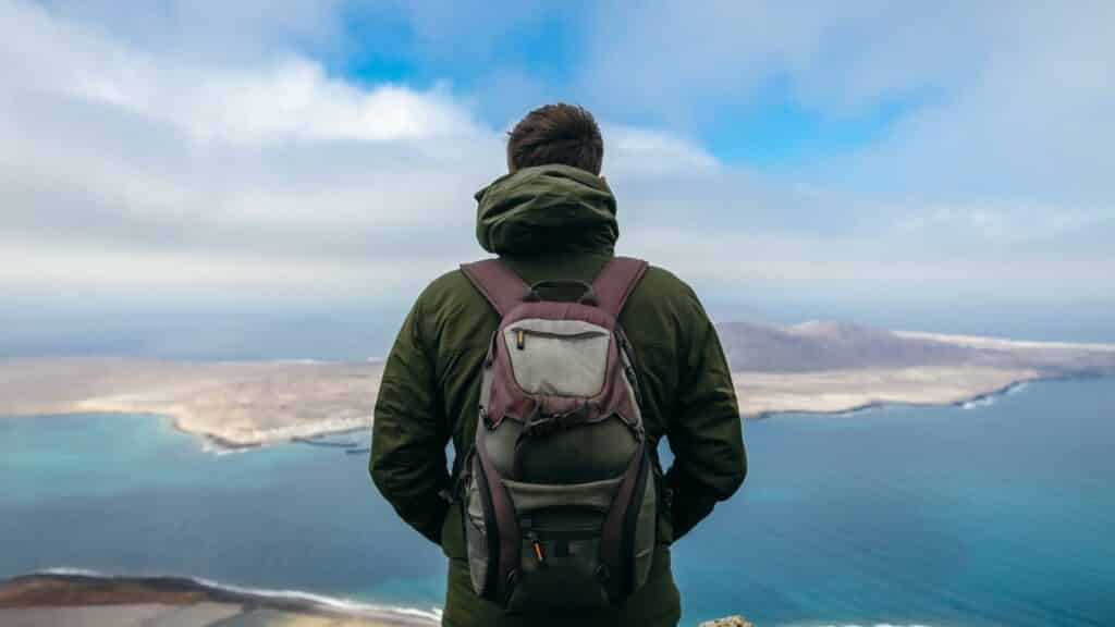 Um homem de mochila contemplando uma ilha.