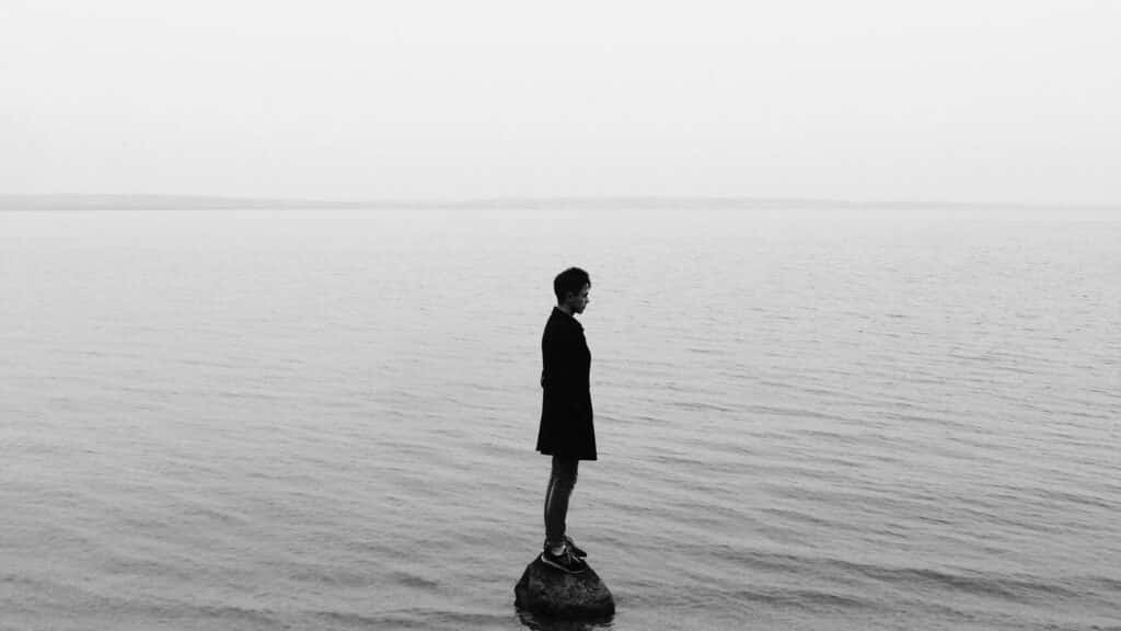 Um homem de pé numa pedra que está ao meio de um grande mar.