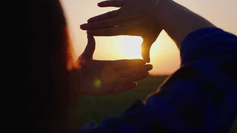 Uma mulher realizando um enquadramento fotográfico com as suas mãos. Ela captura uma luz solar.
