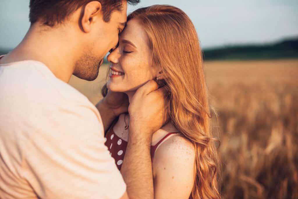 Homem e mulher prestes a se beijar. Ambos estão sorrindo e ao ar livre.