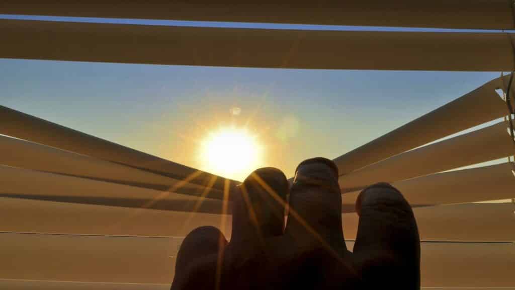 Uma mão abrindo uma janela sobre a qual uma luz solar incide.