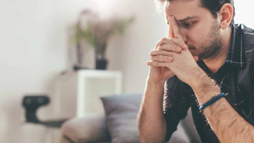 Um homem com semblante preocupado. Ele escora seu rosto nas suas mãos.