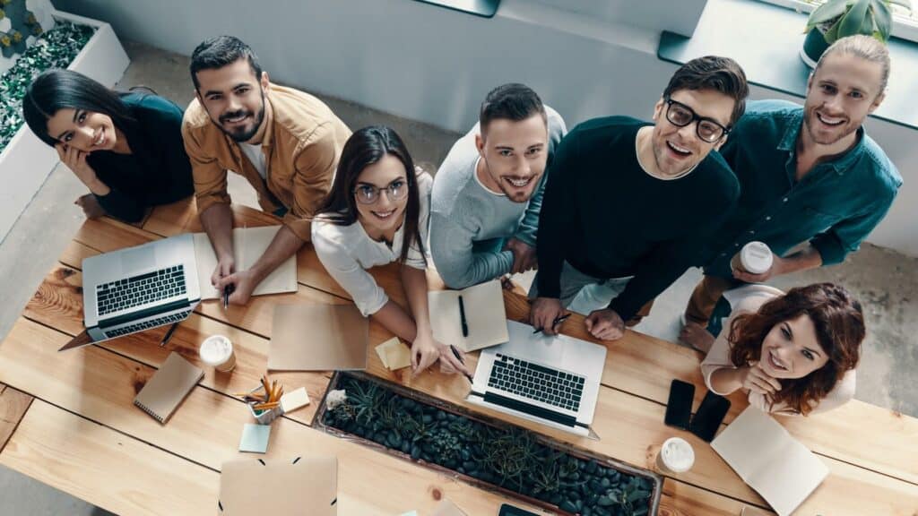 Pessoas num ambiente de trabalho. Numa mesa, vários notebooks.