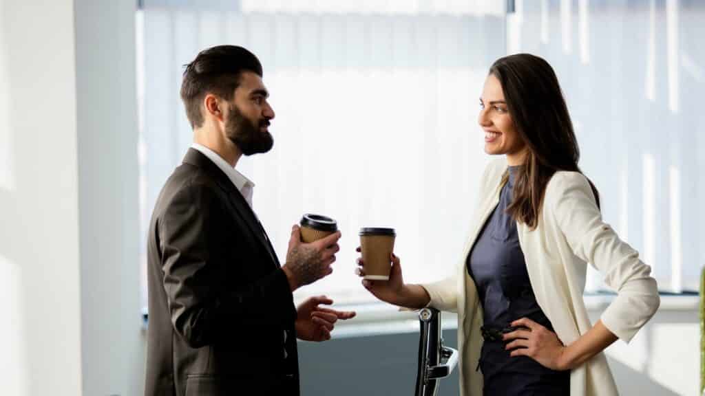 Um homem e uma mulher conversando. Eles seguram copos de café.