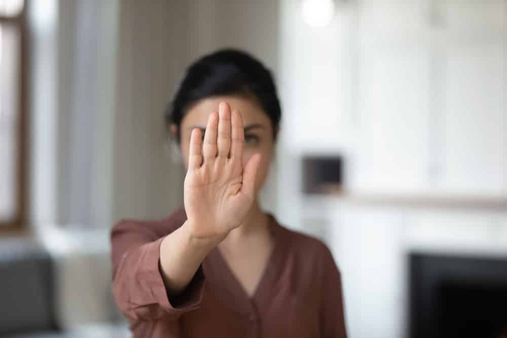 Uma mulher fazendo o sinal de "não" (ou pare) com a mão na frente de seu rosto.