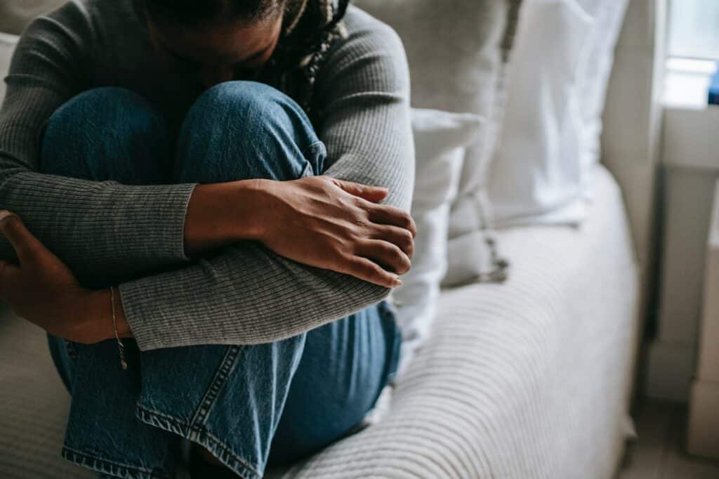 Mulher em posição fetal, em cima da cama, segurando as pernas.