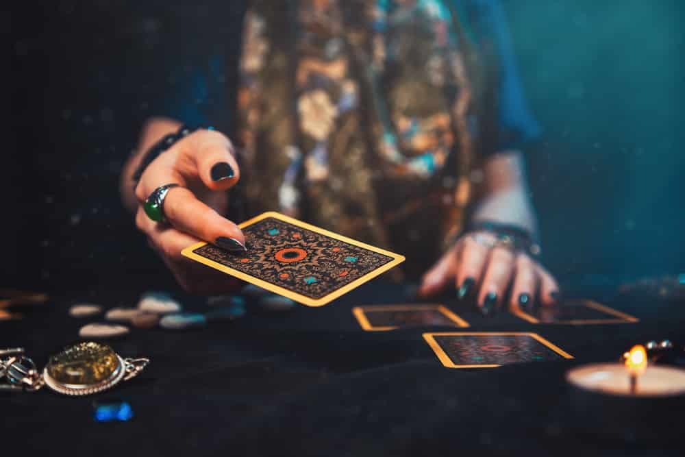 Cartomante em mesa de cartas, com velas e tecidos de estampa esotérica