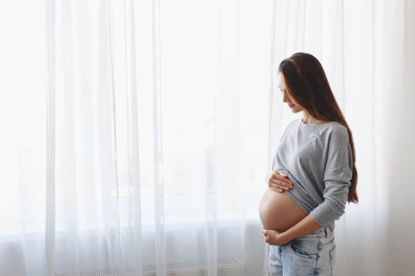 Mulher grávida olhando para a janela enquanto acaricia a barriga