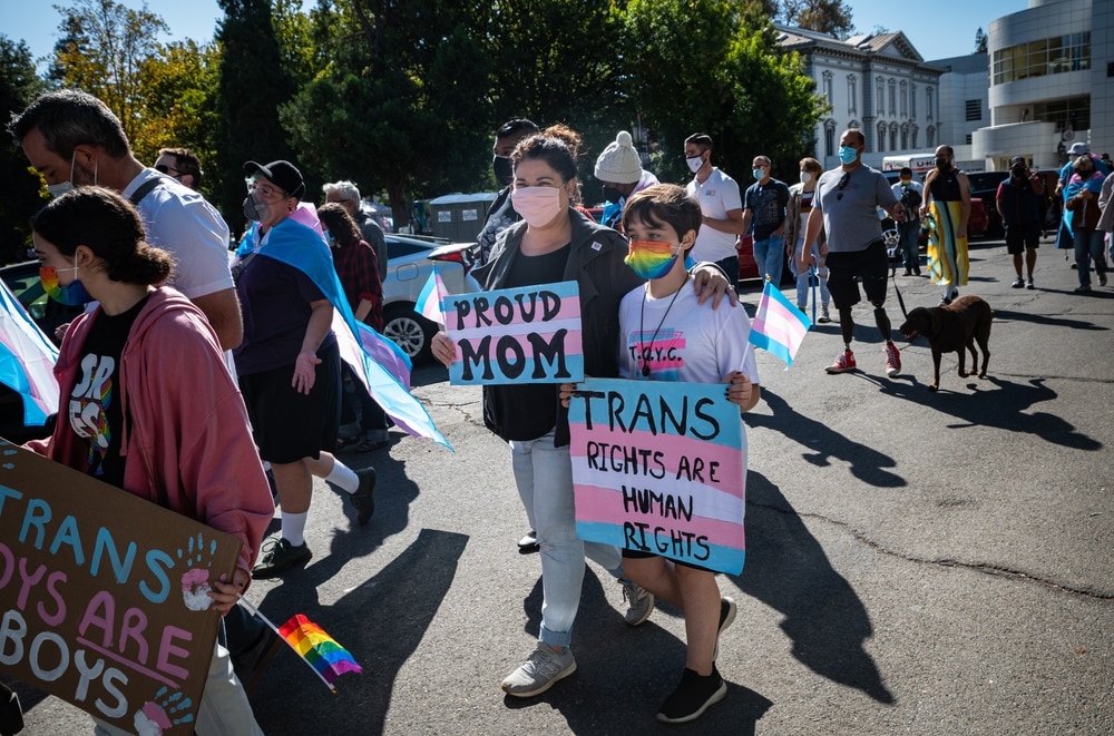 Mãe e filho em passeata LGBTQI+ com placas nas cores da bandeira trans e com o texto "Direitos trans são direitos humanos". 