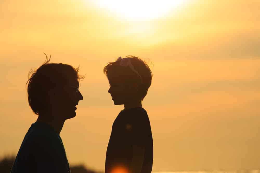 Silhueta de pai e filho pequeno em meio a um céu de pôr do sol