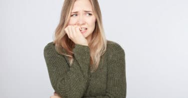 Mulher com blusa verde escura e cara de preocupação roendo as unhas