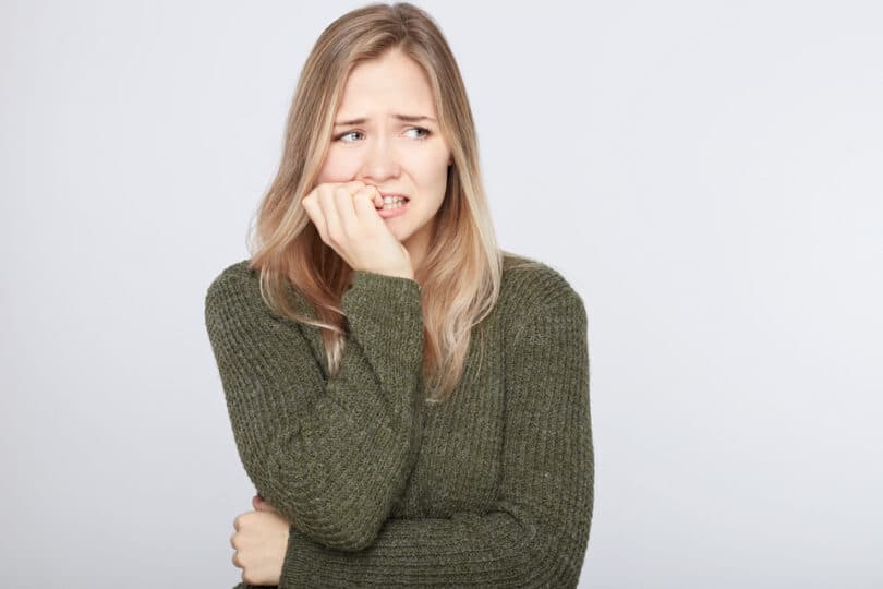 Mulher com blusa verde escura e cara de preocupação roendo as unhas