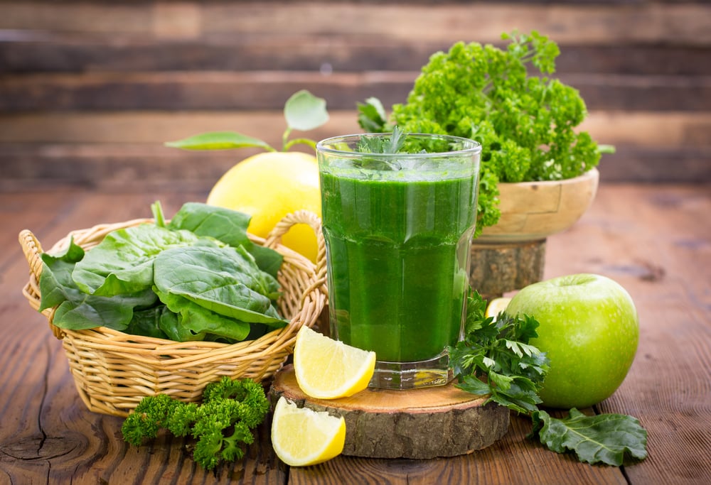 Suco de couve no copo, rodeado por outros ingredientes saudáveis.