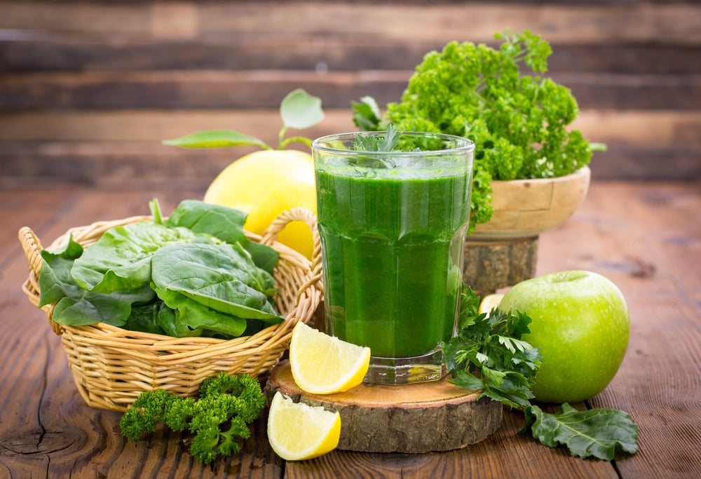 Suco de couve no copo, rodeado por outros ingredientes saudáveis.