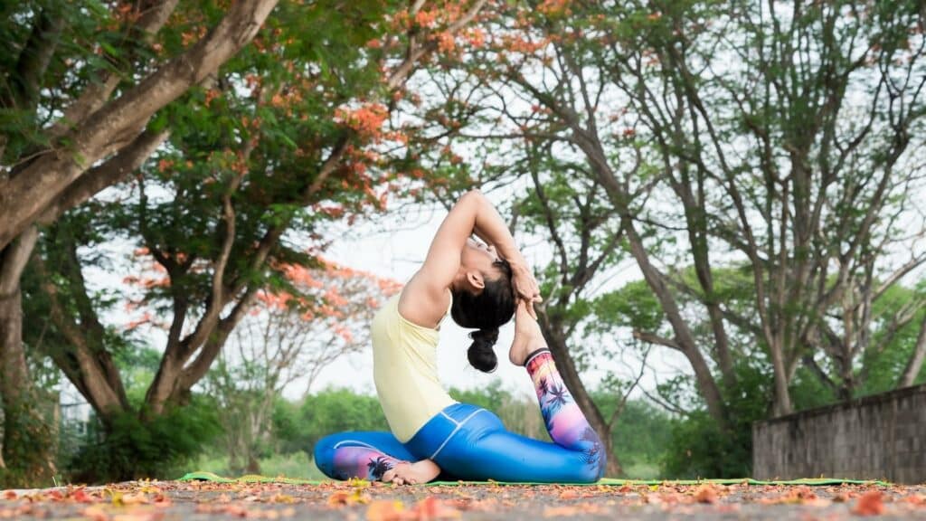 Uma mulher realizando yoga num ambiente repleto de árvores.