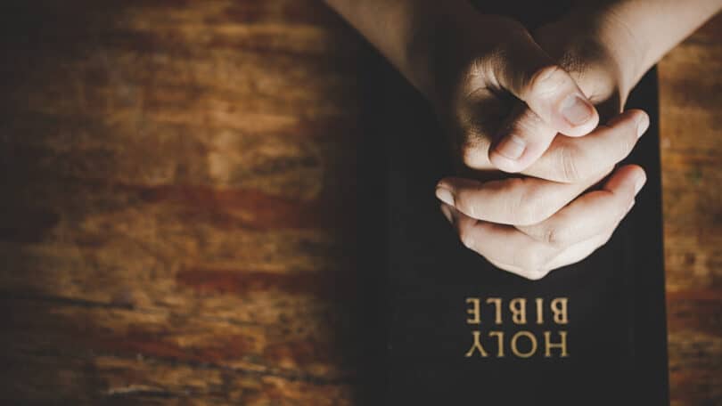 Mãos em gesto de prece/oração postas em cima de uma bíblia.