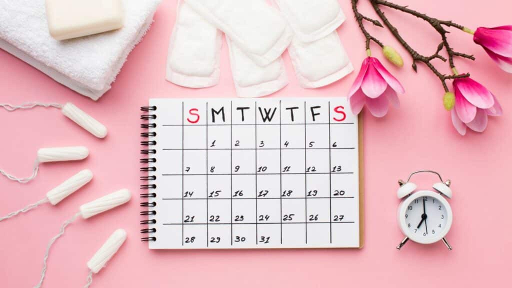 Um calendário. Ao lado, absorventes e, à direita, um despertador.