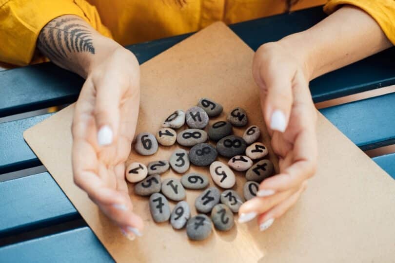 Uma mulher segurando várias pedras que têm números diferentes grafadas nas suas superfícies.