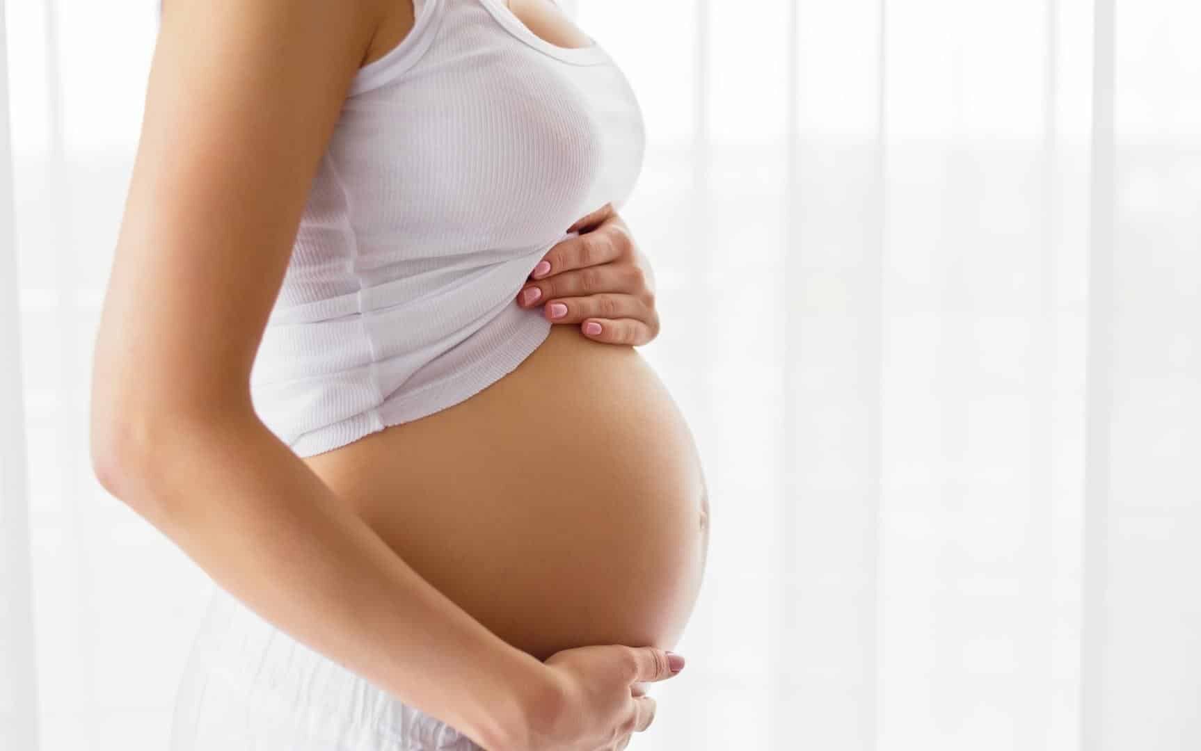 Uma mulher grávida apalpando a sua própria barriga.