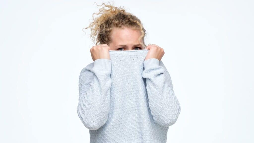 Uma mulher escondendo o seu rosto (preocupado) por baixo de um suéter.