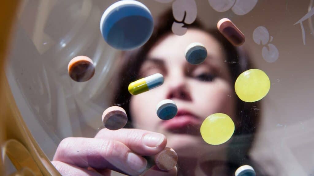 Uma mulher selecionando uma pílula de remédio de entre várias postas na superfície de um plástico.