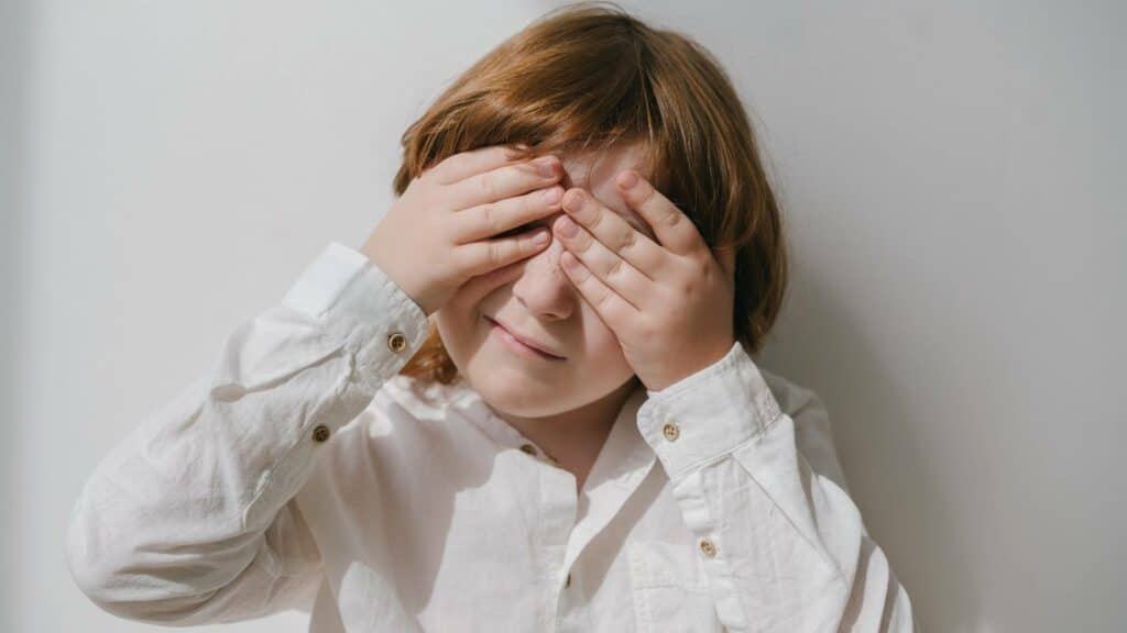 Uma criança tapando os seus olhos com as mãos.